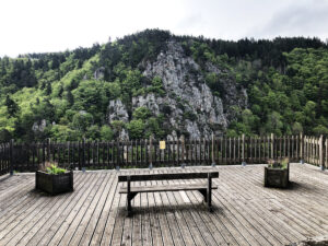 View from Saint-Privat: a wooden lookout point with a bench overlooks a tree-covered mountain